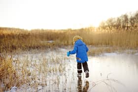 Preschool boy is playing on the ice of a frozen lake or river on a cold sunny winter sunset. Child sliding and having fun with during family hiking. Kids outdoor games in winter