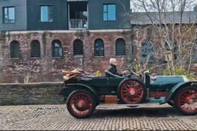 An antique car driving down a cobbled street