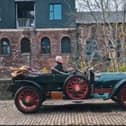 An antique car driving down a cobbled street