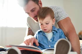 Attractive father teaching cute child daughter reading and writing skills through loving parenting, while lying on cosy bed in bright modern home