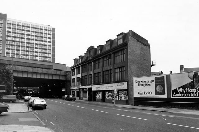 Neville Street showing the railway bridge on the left, with City House towering behind in November 1980. In the centre are Neville Motors, used car dealers and the Carpet and Dry Cleaning Centre. Advertising hoardings on the right including one for Sovereign cigarettes.