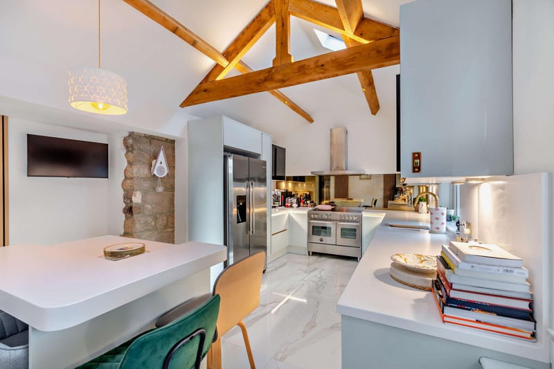 A modern breakfast kitchen with exposed beams and feature stone wall.