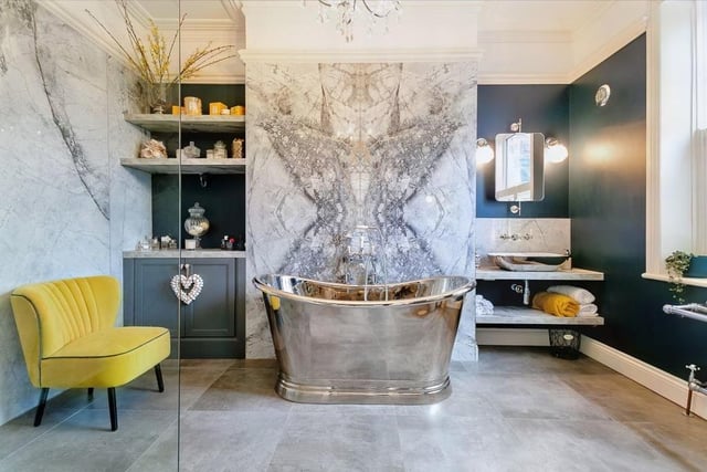 A luxury en suite bathroom has a heated, porcelain tiled floor with a free standing metal roll top bath, walk-in rain shower and vanity wash basin with lights.