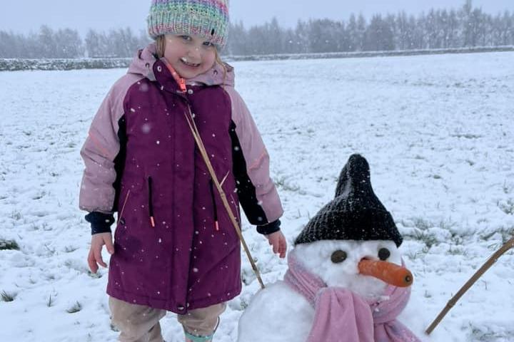 A youngster wrapped up and enjoying building a snowman this afternoon