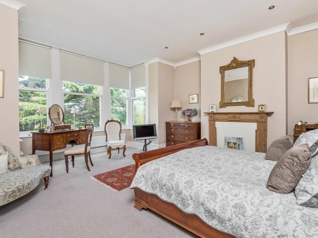 An impressive bedroom with a large bay window allowing natural light to flood in, and a feature fireplace.