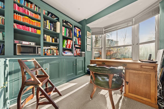 A well-lit study has fitted bookshelves with cupboards beneath,