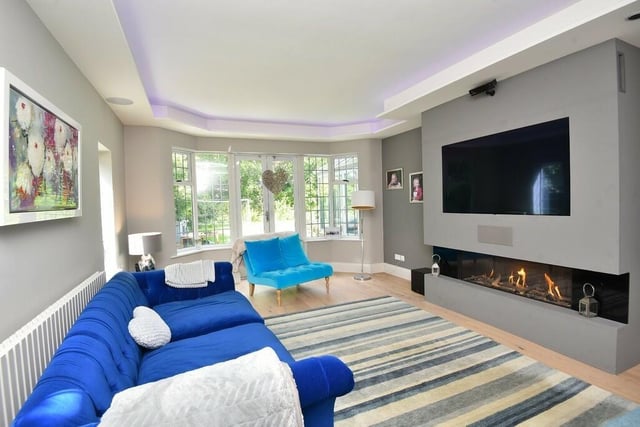 A stunning living room has a contemporary, wall-mounted living flame gas fire, a built-in television and surround sound.