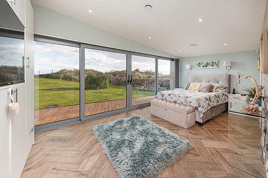 To the main ground floor is a master bedroom suite, which is beautifully positioned with large glazed aspect over the gardens and terrace towards the beach, and benefits from bespoke fitted furniture.