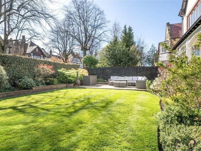 A stretch of lawned garden with filled borders and patio seating area.