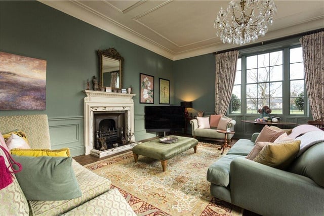 The large sitting room with feature fireplace and period decorative detail. Double aspect windows look over the grounds and tennis courts.