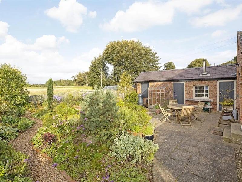 A patio seating area and gardens flanked by open fields.