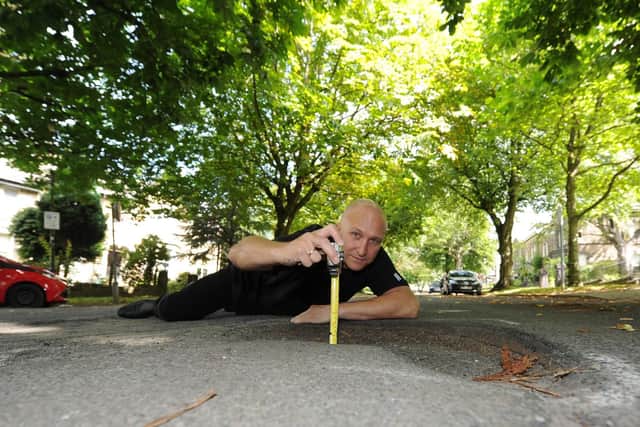 Resident Phil Standen measuring the depth of one of the potholes. Picture: Gerard Binks.