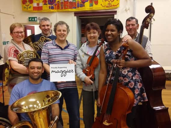 HSO musical director Bryan Western holds up the Maggies charity logo with members of the orchestra.
